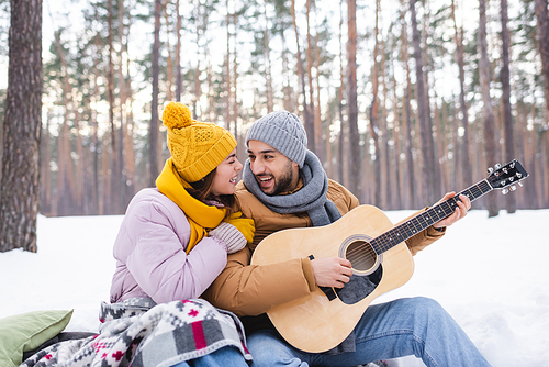 Happy couple playing acoustic guitar on snow in winter park