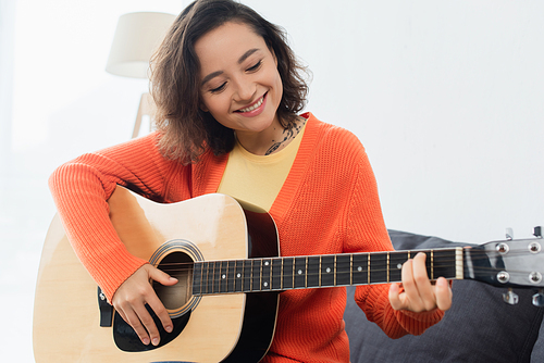 happy young woman playing acoustic guitar at home