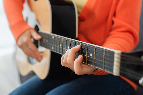 cropped view of young woman playing acoustic guitar at home