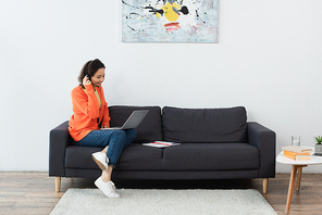 cheerful operator in headset using laptop while sitting on sofa