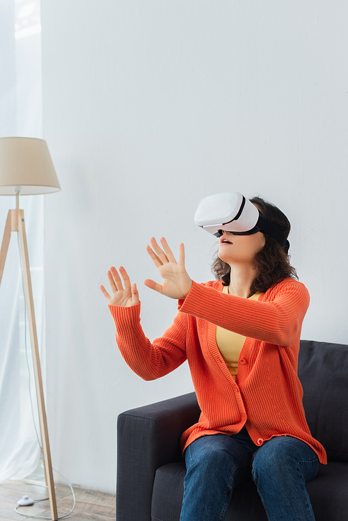 young brunette woman in vr headset gesturing while playing and sitting on sofa