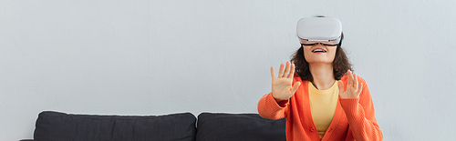 young happy woman in vr headset gesturing during simulation game at home, banner
