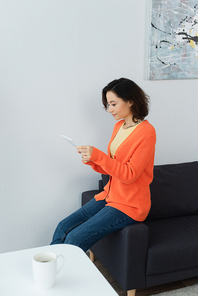 young woman using digital tablet and leaning on couch