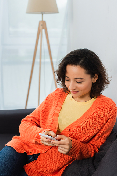 happy young woman texting on cellphone in living room