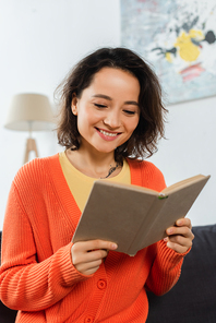 happy and tattooed woman reading book at home