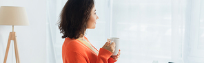 side view of pleased young woman holding mug at home, banner