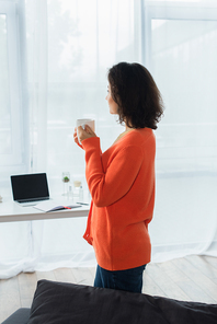 side view of young woman holding cup of coffee at home