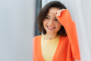 portrait of joyful young woman smiling near white curtain