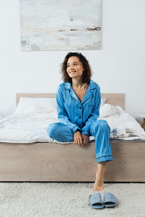 happy tattooed woman in pajamas sitting on bed