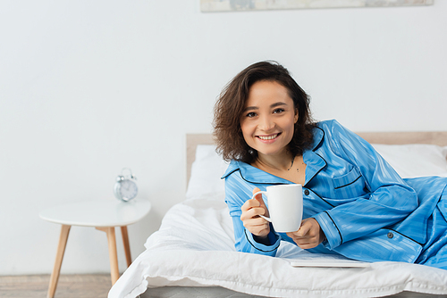 happy young woman in blue pajamas holding cup of . at home