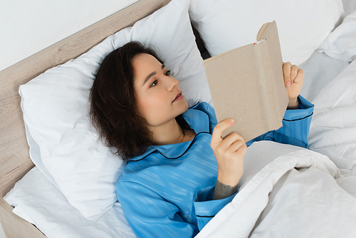 high angle view of brunette woman reading book in bed