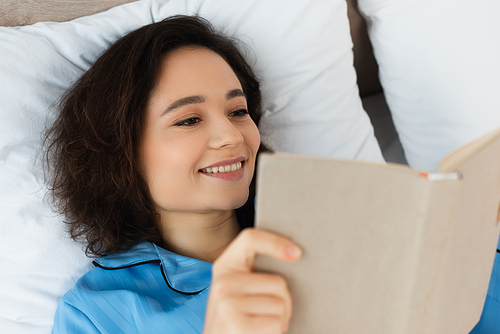 high angle view of cheerful young  woman reading book in bed