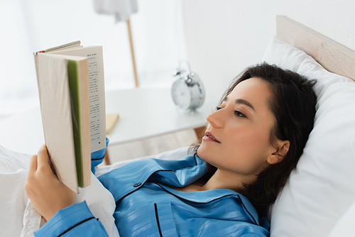 young woman in blue pajamas reading book in bed