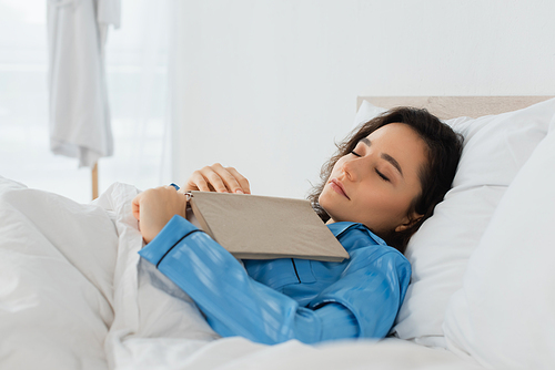young woman in blue pajamas sleeping with book in bed