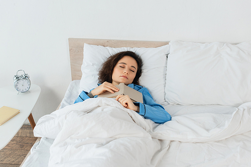 brunette woman in blue pajamas sleeping with book in bed