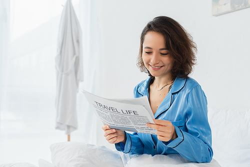 happy woman in blue pajamas reading travel life newspaper in bed