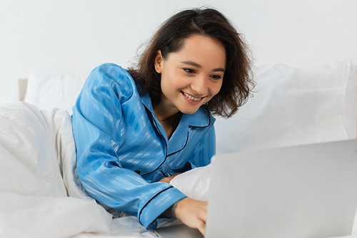 smiling young freelancer in pajamas using laptop in bedroom