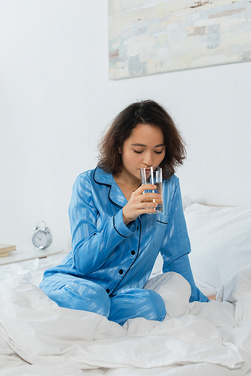 young woman in blue pajamas holding glass of water in bedroom