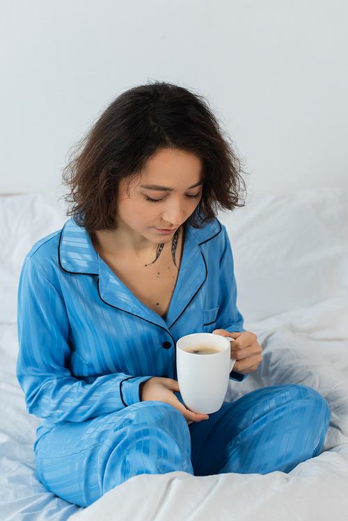young woman in blue pajamas holding cup of coffee in bedroom