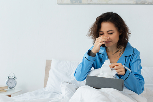 sick woman with running nose reaching tissue box in bed