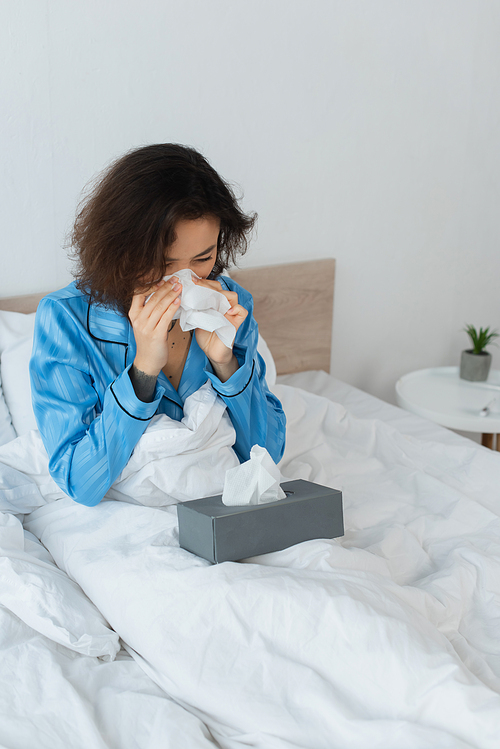 sick woman sneezing in tissue in bedroom