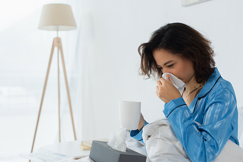 sick woman sneezing in napkin while holding cup of .