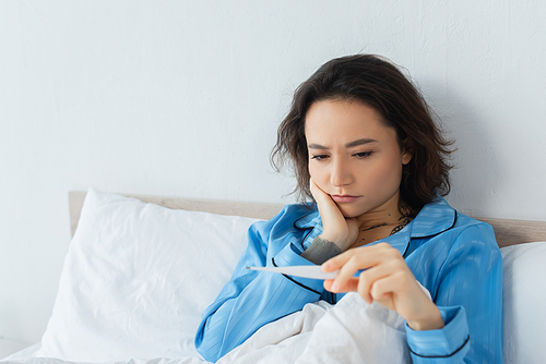 sick young woman looking at electronic thermometer