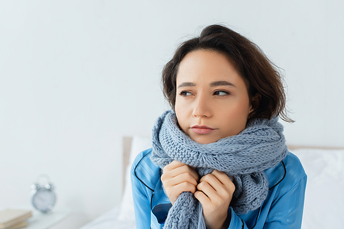young woman in knitted scarf looking away at home