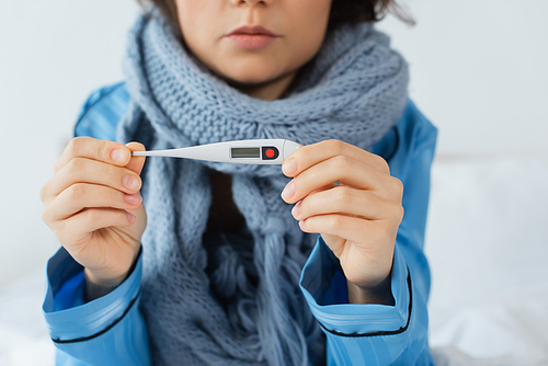 cropped view of sick young woman in knitted scarf holding electronic thermometer