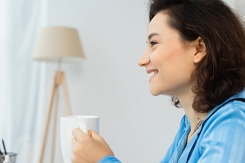 side view of happy young woman holding cup of coffee