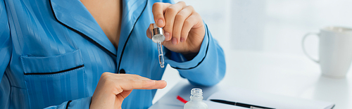 cropped view of young woman holding pipette with oil near fingernails, banner