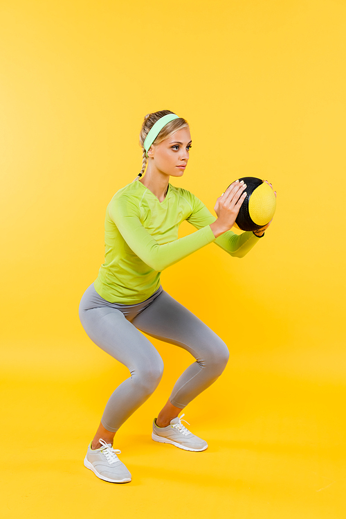 full length view of slim woman in grey leggings doing sit ups with ball on yellow