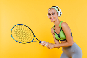 smiling sportswoman in headphones playing tennis isolated on yellow