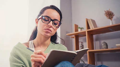 Student in eyeglasses writing on notebook in living room