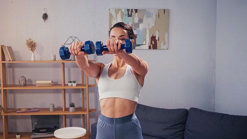 Fit sportswoman working out with dumbbells at home