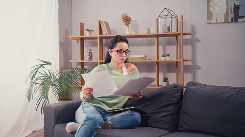 Student in eyeglasses looking at papers while sitting on couch