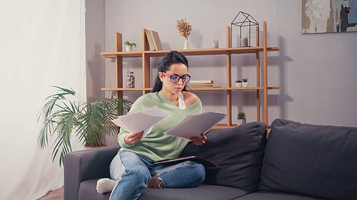 Focused student looking at papers on couch in living room