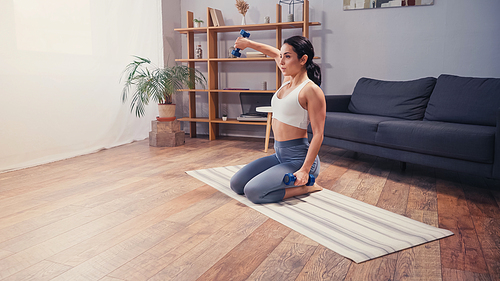 Athletic sportswoman exercising with dumbbells on fitness mat at home