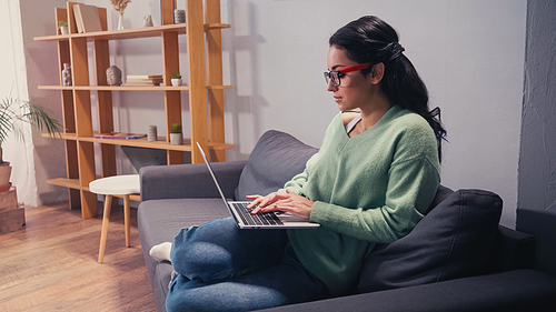 Side view of pretty freelancer using laptop on couch