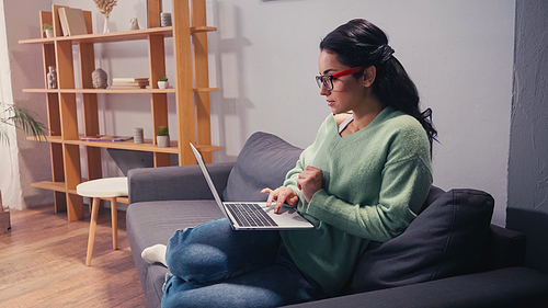 Side view of woman in eyeglasses working on laptop at home