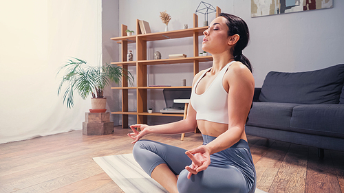 Athletic woman meditating on yoga mat in living room