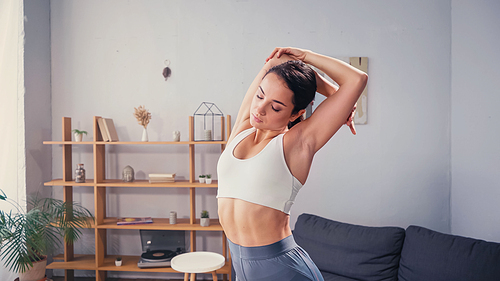 Pretty woman with closed eyes in sportswear stretching at home