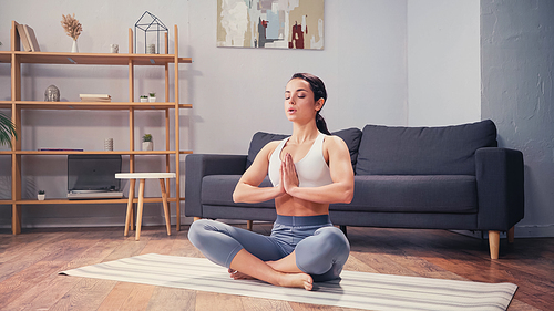 Barefoot woman meditating on yoga mat at home