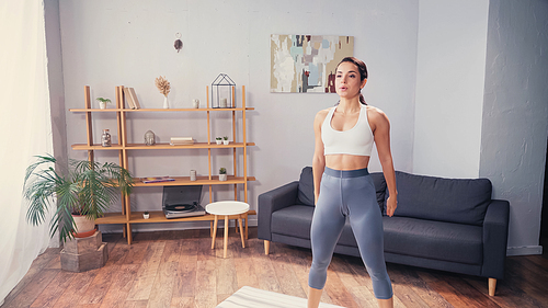 Brunette woman in sportswear standing on fitness mat at home