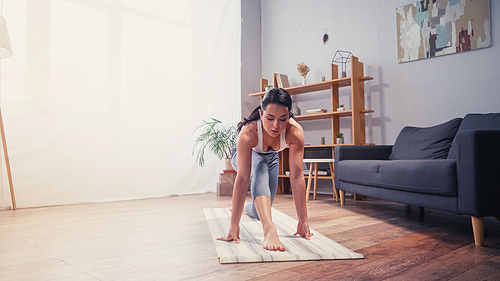Sportswoman exercising near couch on fitness mat at home