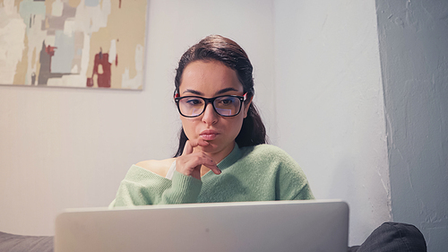 Pensive freelancer looking at blurred laptop at home