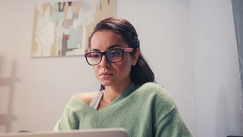 Young freelancer in eyeglasses looking at blurred laptop