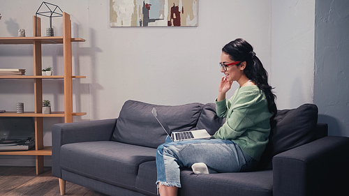 Side view of smiling freelancer having video chat on laptop at home