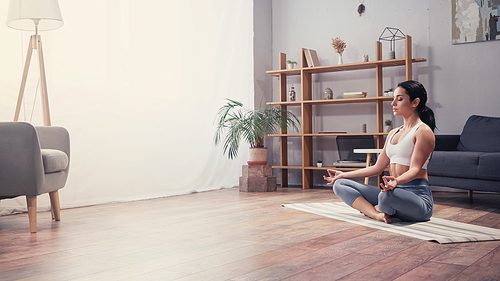 Side view of young woman meditating in living room