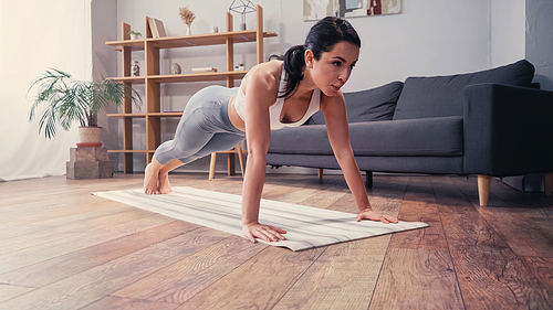 Sportswoman doing press ups on fitness mat near couch at home